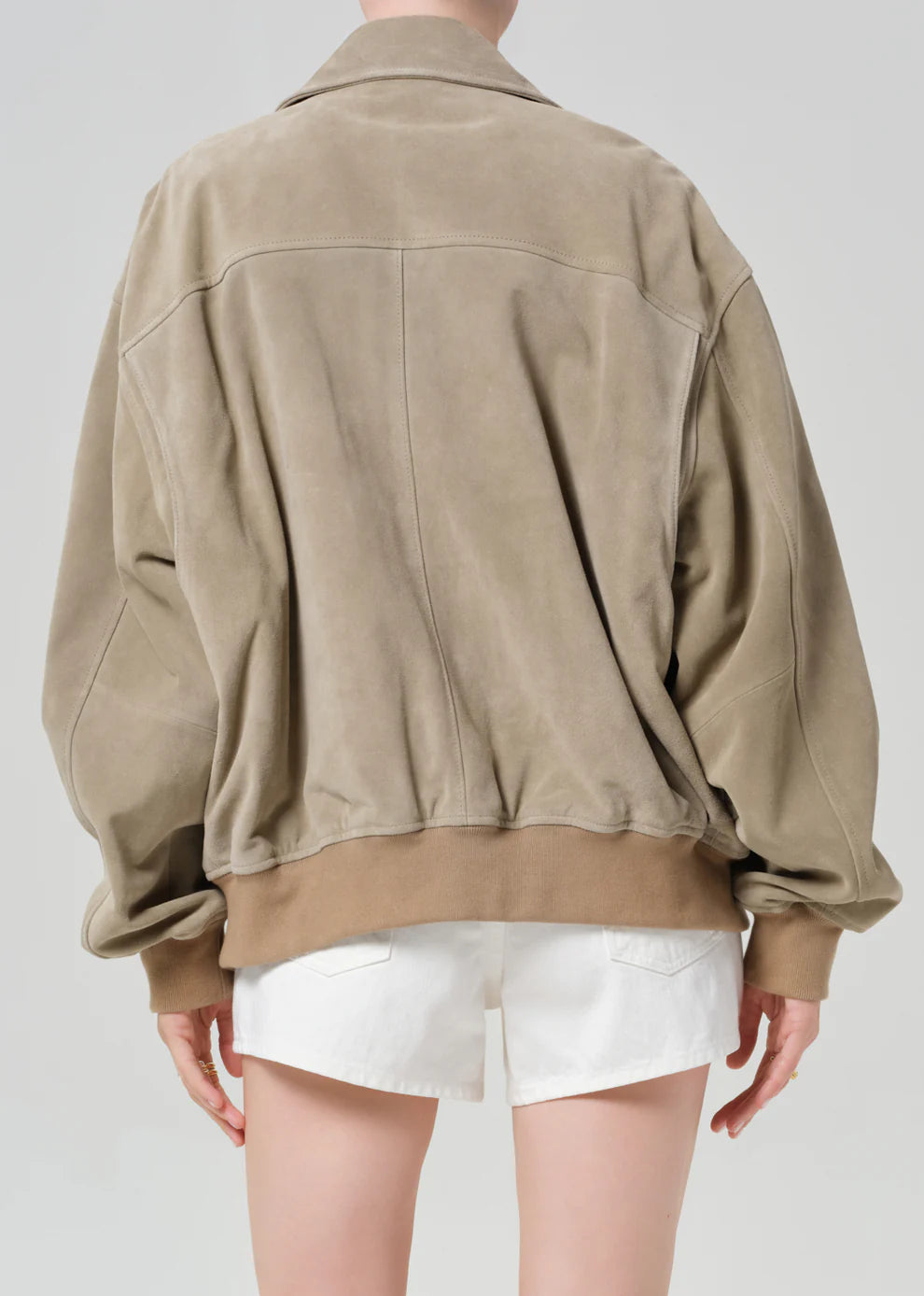 Person wearing a beige jacket and white shorts on a plain background