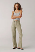 Woman wearing a gray tank top and beige pants on a plain background