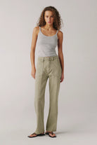 Woman wearing a light gray tank top and beige pants on a plain background