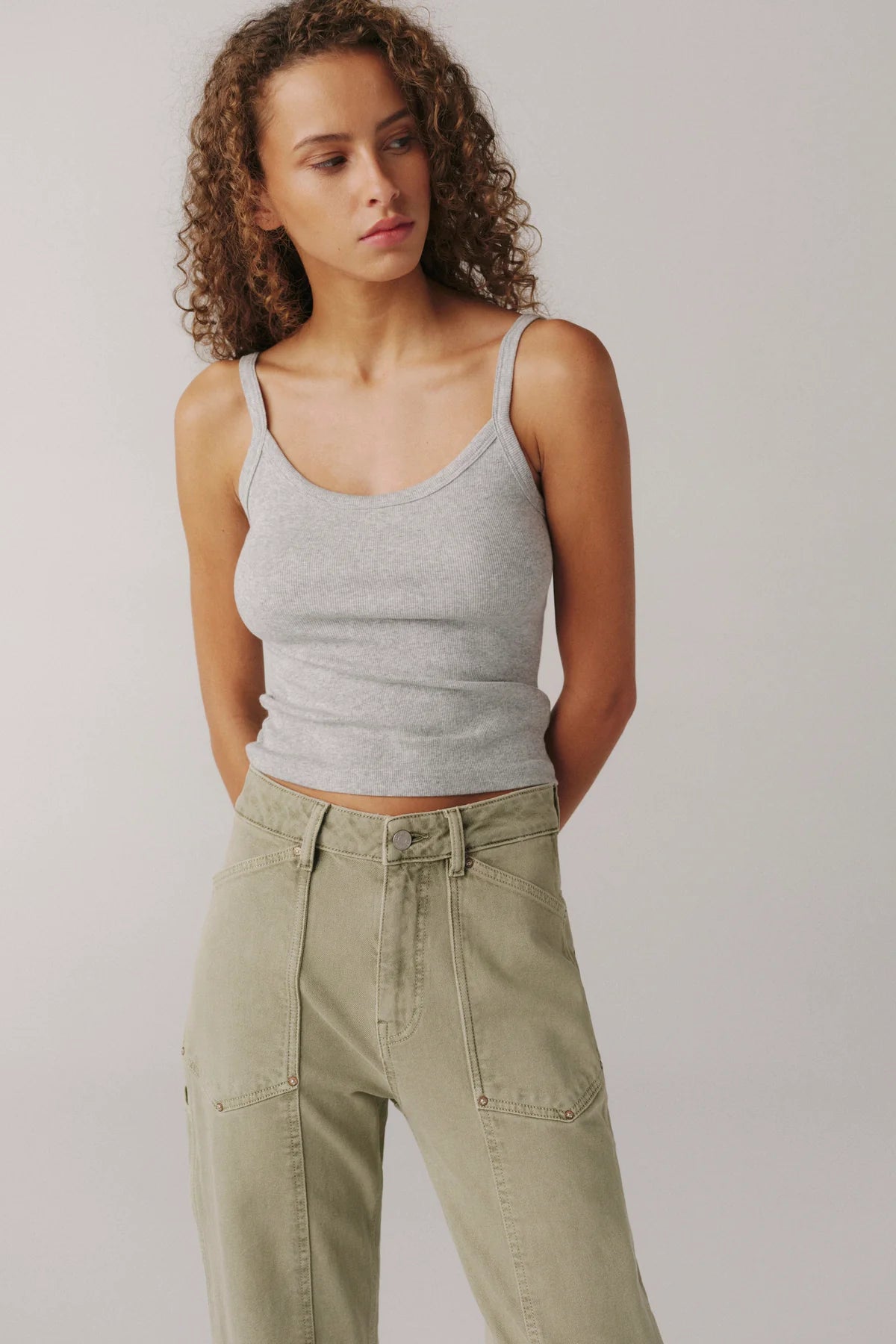 Woman wearing a gray tank top and green pants against a plain background