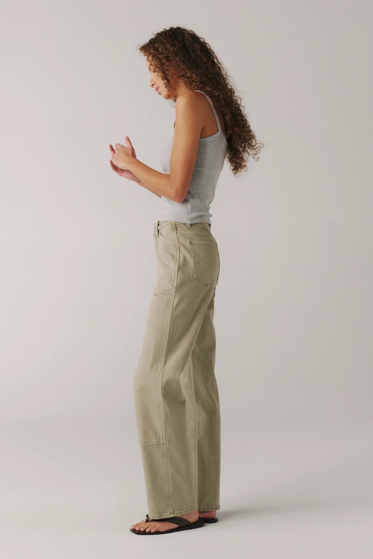Woman wearing light green pants and a gray top on a plain background