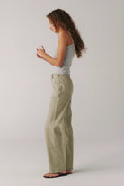 Woman wearing light green pants and a gray top on a plain background