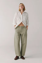 Person wearing a white shirt and green pants on a plain background