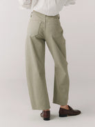 Person wearing light green pants and a white shirt on a plain background