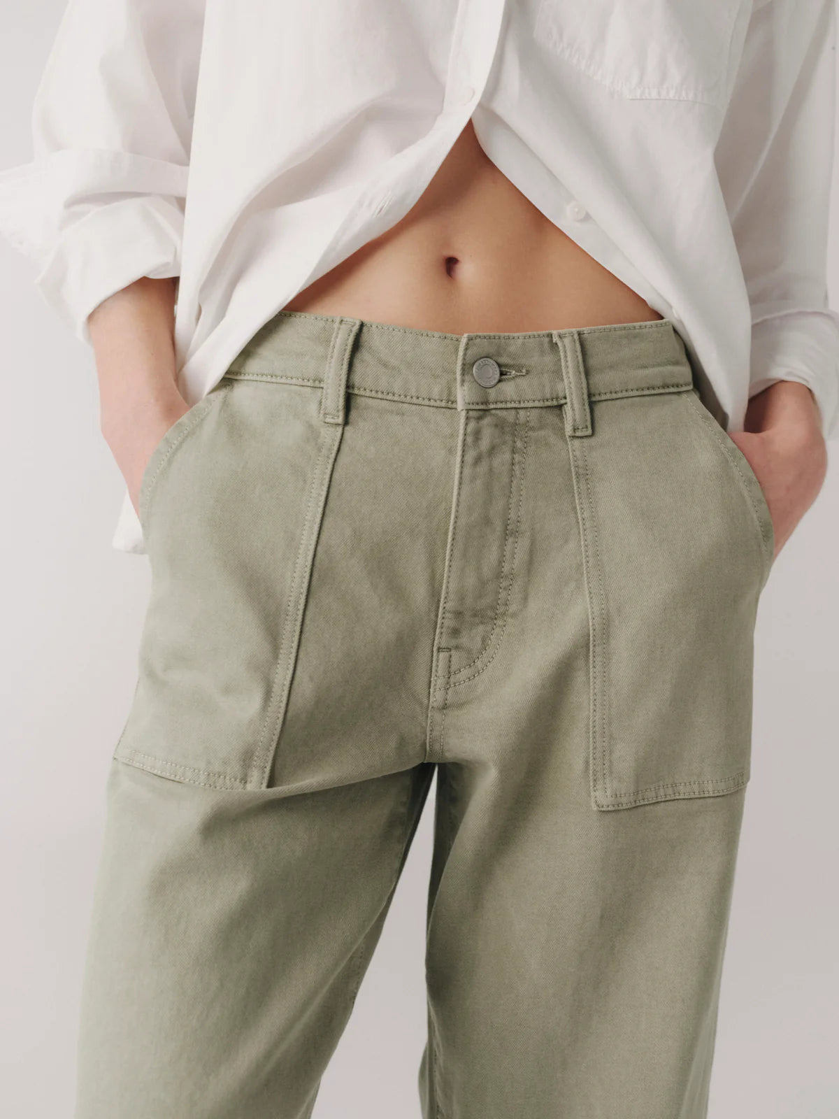 Person wearing light green pants and a white shirt against a plain background