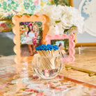 Clear container with blue matches on a decorative table with floral arrangements and photo frames.