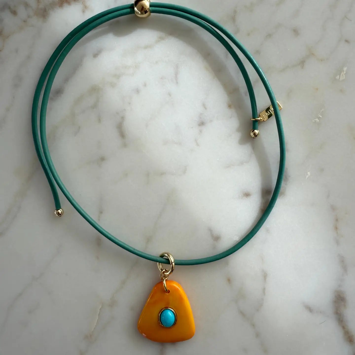 Green necklace with a yellow pendant featuring a blue stone on a marble surface