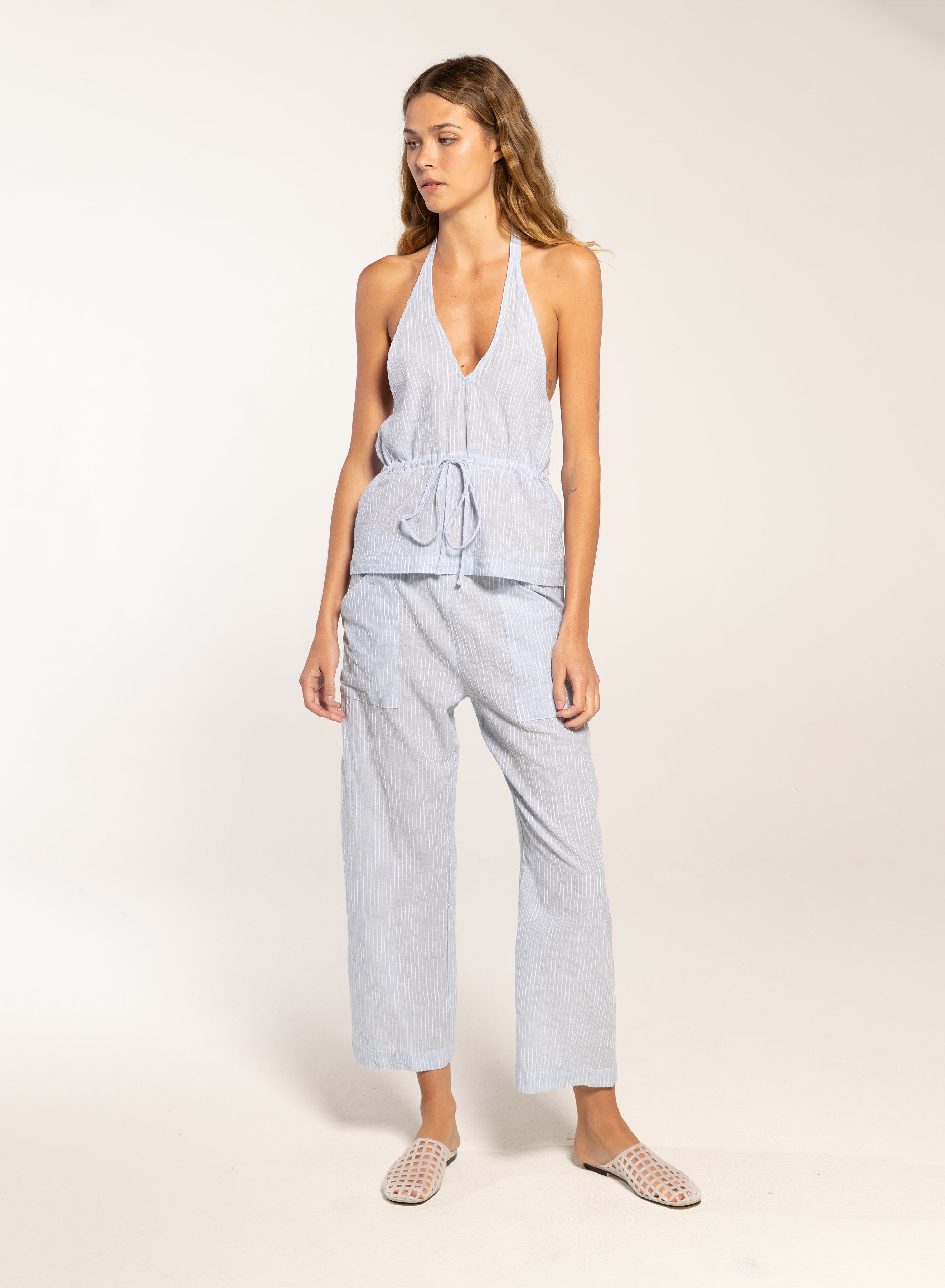 Woman wearing a light blue sleeveless top and pants on a white background
