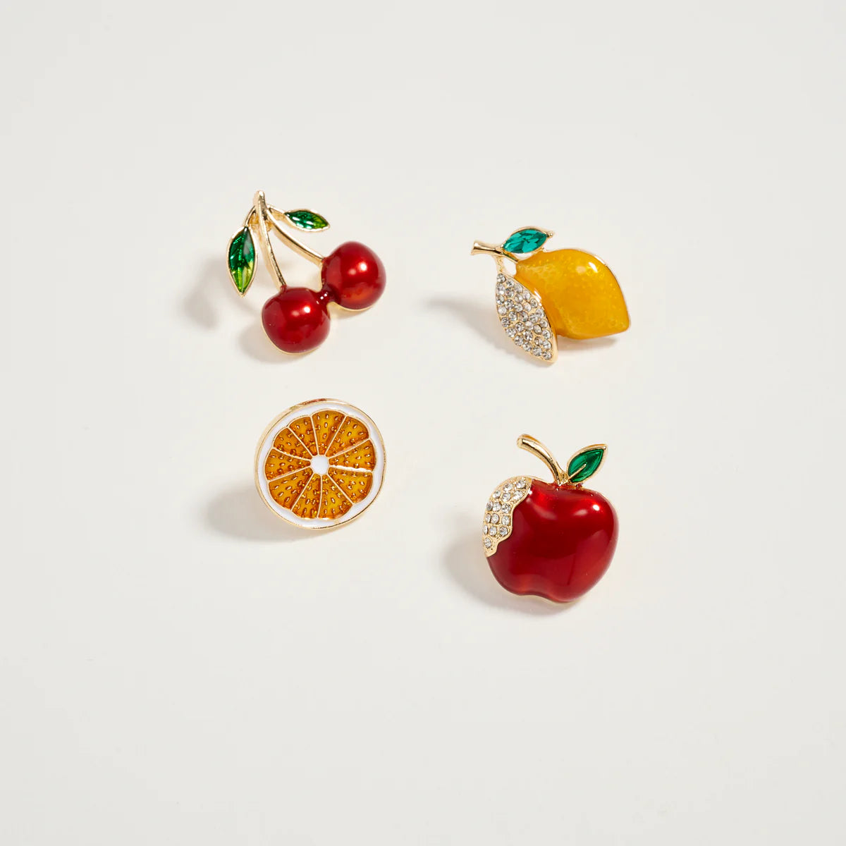 Four fruit-themed earrings on a light gray background