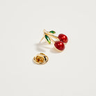 Gold earring with red cherries on a light gray background