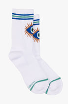 A pair of white crew socks with blue and green stripes at the cuff, featuring a stylized embroidered eye design on the side, and a green toe stripe. The brand name 'STOCKHOLM' is printed near the heel.