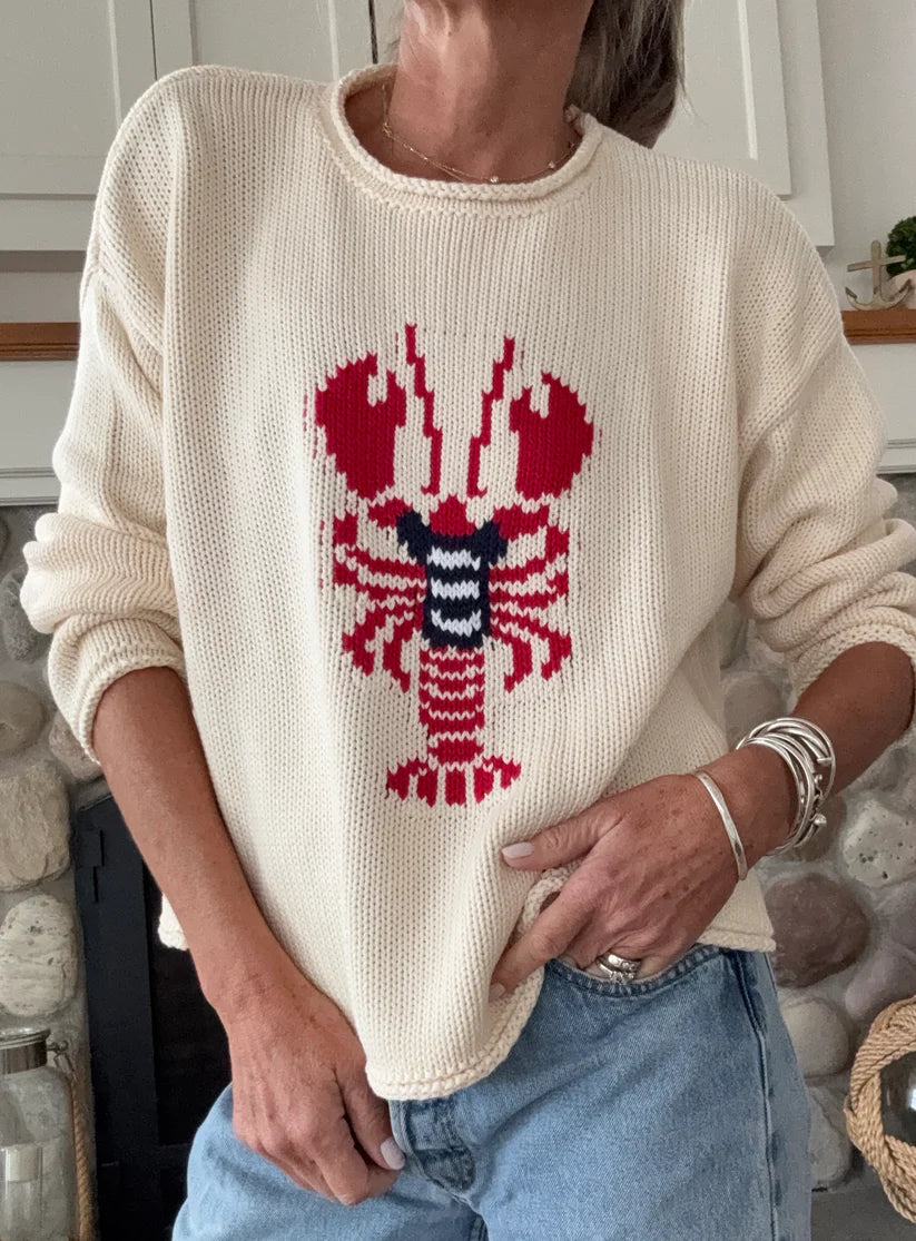 Person wearing a cream sweater with a red and blue lobster design, standing in a casual setting.
