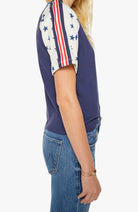 Person wearing a navy blue sleeveless top with a patterned shoulder and blue jeans on a white background