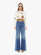 Woman wearing a sweater with embroidered designs and blue jeans on a white background