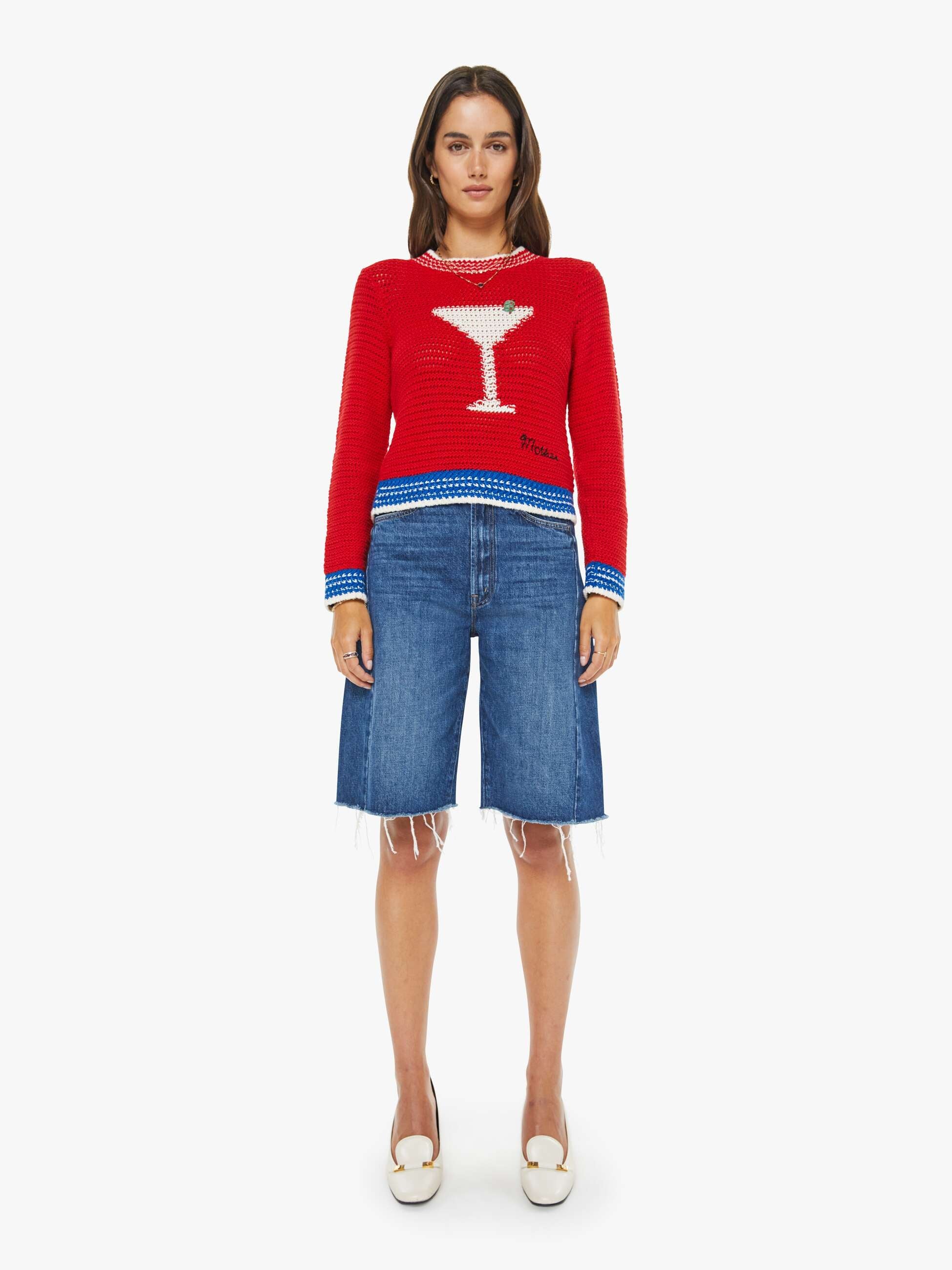 Woman wearing a red sweater with a martini glass design and blue denim shorts on a white background