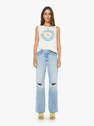 Woman wearing a sleeveless top with a circular design and light blue jeans on a white background