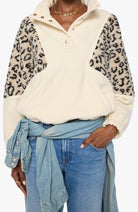 A person wearing a cream-colored fleece pullover with leopard-print faux fur sleeves, styled with a light blue denim shirt tied around the waist and blue jeans.