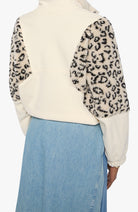 A cropped fleece pullover jacket with a cream body and leopard-print faux-fur sleeves, shown from the back on a model wearing a light blue denim skirt.