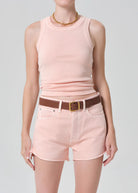 Person wearing a pink sleeveless top and shorts with a brown belt on a gray background