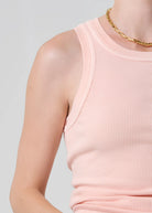 Person wearing a light pink ribbed tank top on a gray background