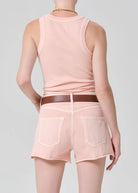 Person wearing a pink sleeveless top and shorts with a brown belt on a light gray background