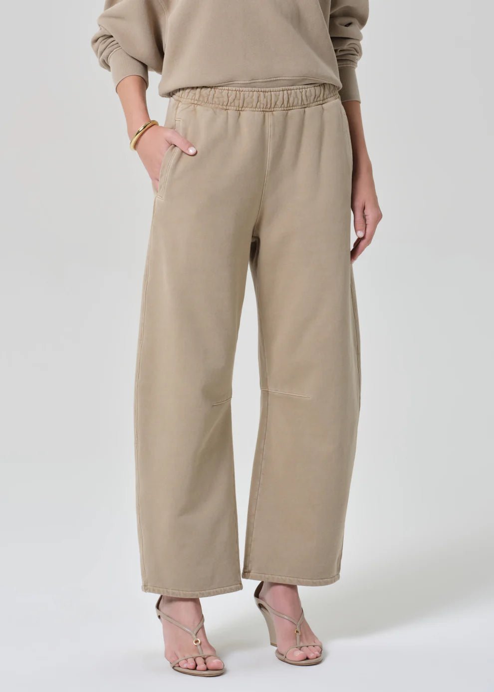 Person wearing beige pants and a matching top on a white background