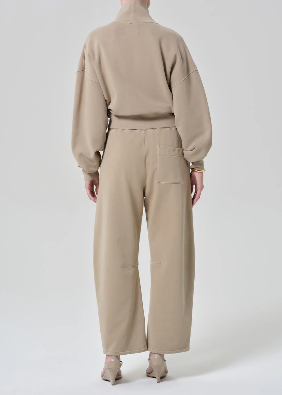 Person wearing a beige outfit with a sweater and pants on a white background