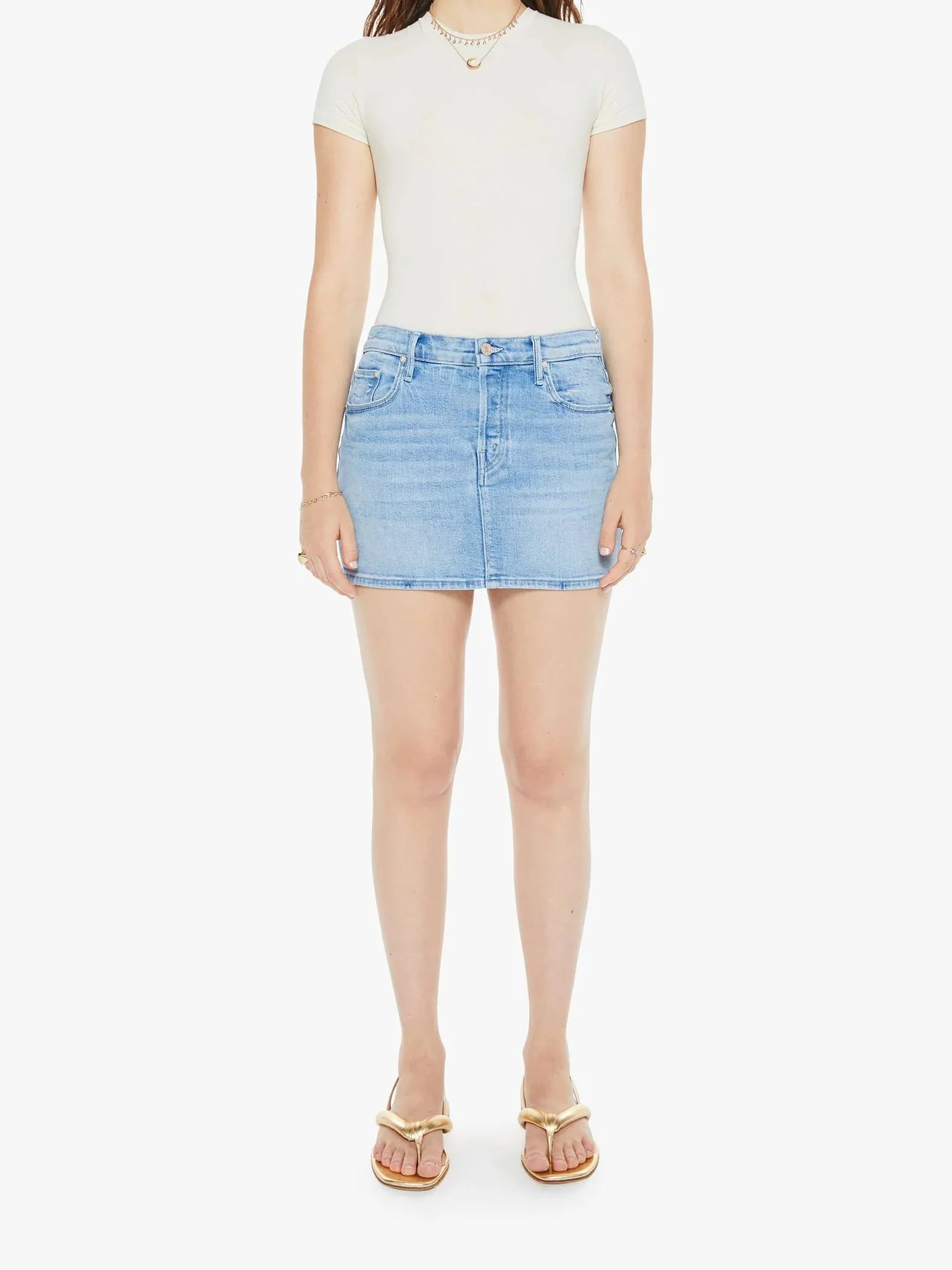 A woman is standing, wearing a white top and a light blue denim mini skirt with a thigh-grazing hem. She has sunglasses on and is posing against a white background.