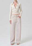 Person wearing a cream-colored outfit with a cardigan and wide-leg pants on a white background