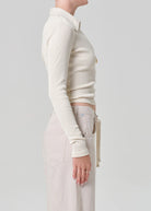 Person wearing a cream-colored long-sleeve top and light-colored pants on a plain background
