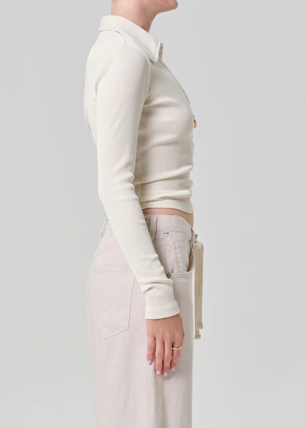 Person wearing a cream-colored long-sleeve top and light-colored pants on a plain background
