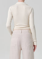 Person wearing a cream ribbed sweater and light-colored pants on a plain background