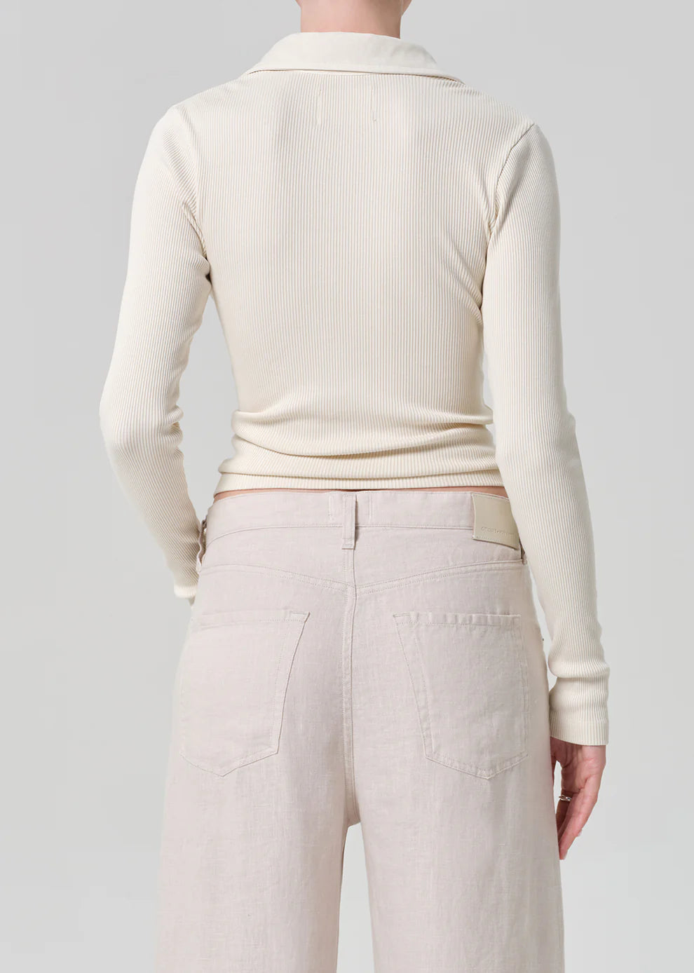 Person wearing a cream ribbed sweater and light-colored pants on a plain background