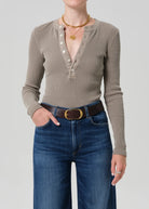Person wearing a brown long-sleeve henley shirt and blue jeans on a plain background