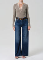 Person wearing a beige long-sleeve top and blue jeans on a white background