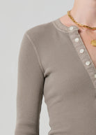 Close-up of a person wearing a brown textured long-sleeve top with a plain background