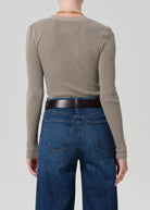 Person wearing a beige long-sleeve shirt and blue jeans on a plain background