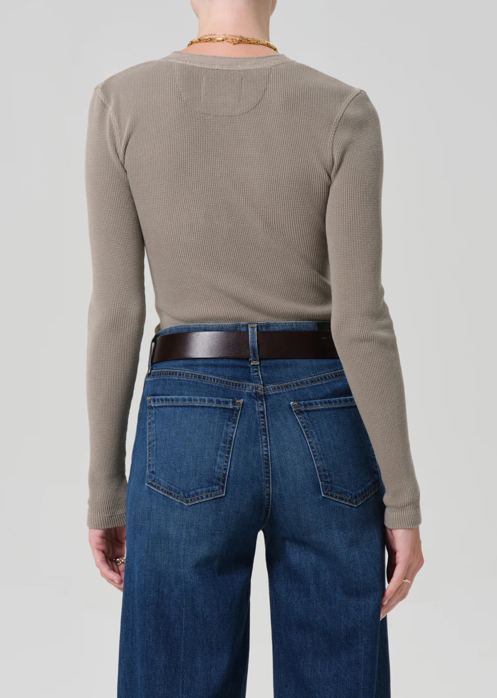 Person wearing a beige long-sleeve shirt and blue jeans on a plain background