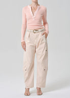 Person wearing a pink sweater and beige pants on a white background