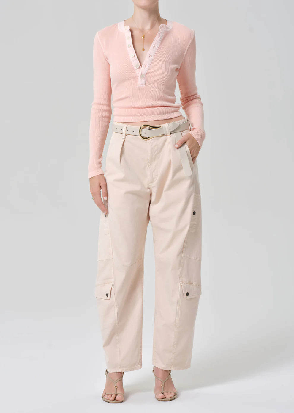 Person wearing a pink sweater and beige pants on a white background