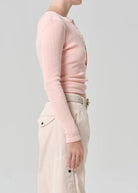 Person wearing a light pink long-sleeve top and beige pants on a plain background