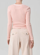 Person wearing a light pink long-sleeve top and beige pants on a gray background