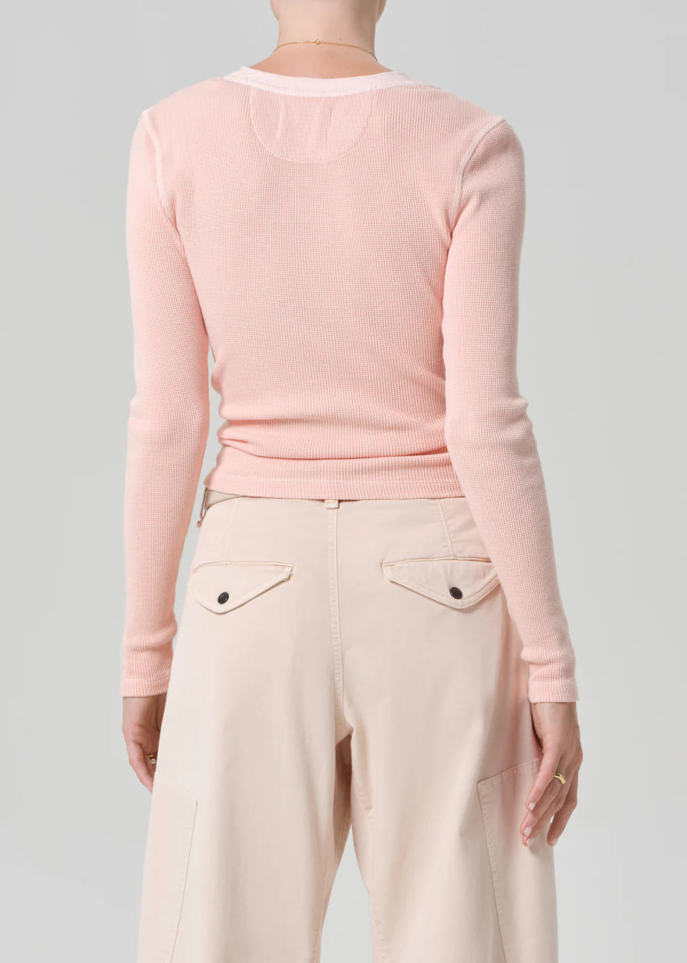 Person wearing a light pink long-sleeve top and beige pants on a gray background