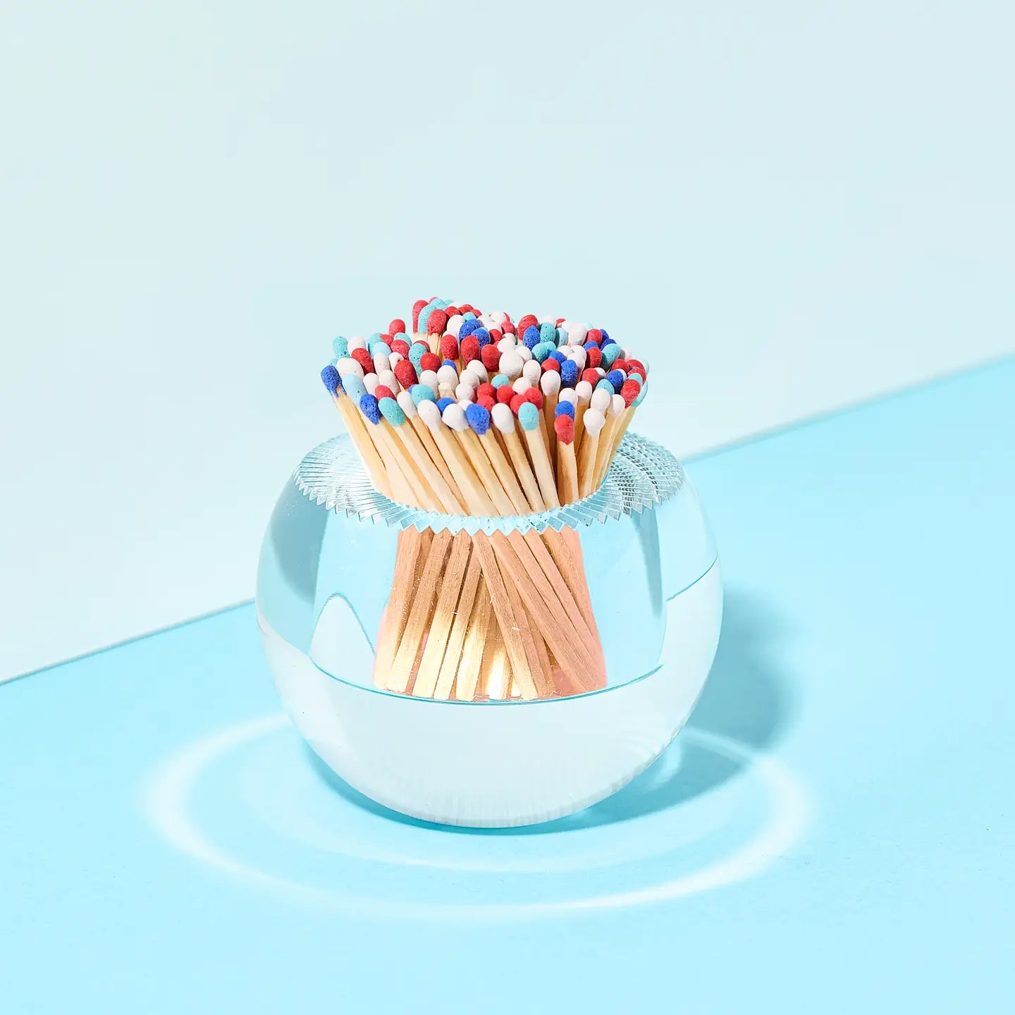 Clear glass container with colorful matches on a light blue background