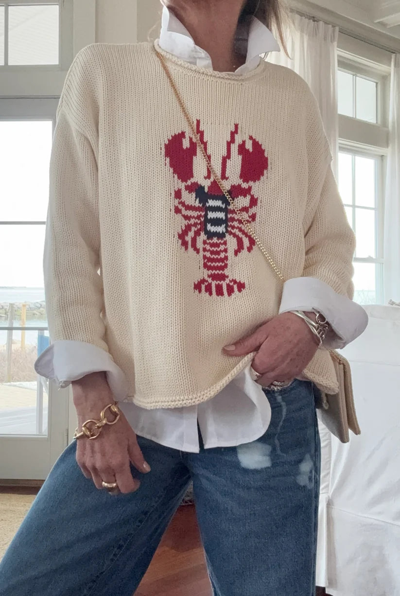 Person wearing a cream sweater with a lobster design, standing indoors.