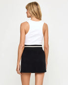 Woman wearing a white sleeveless top and black skirt on a plain background