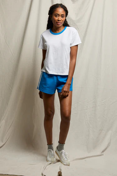 Person wearing a white t-shirt with blue trim and blue shorts against a plain background