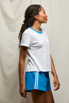 Person wearing a white t-shirt with blue trim and blue shorts against a neutral background