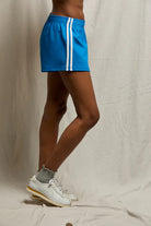 Person wearing a blue athletic skirt with white stripes on a neutral background