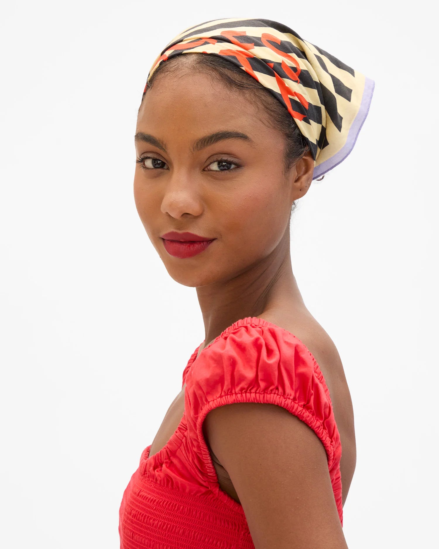 Woman wearing a colorful headscarf and red top on a white background